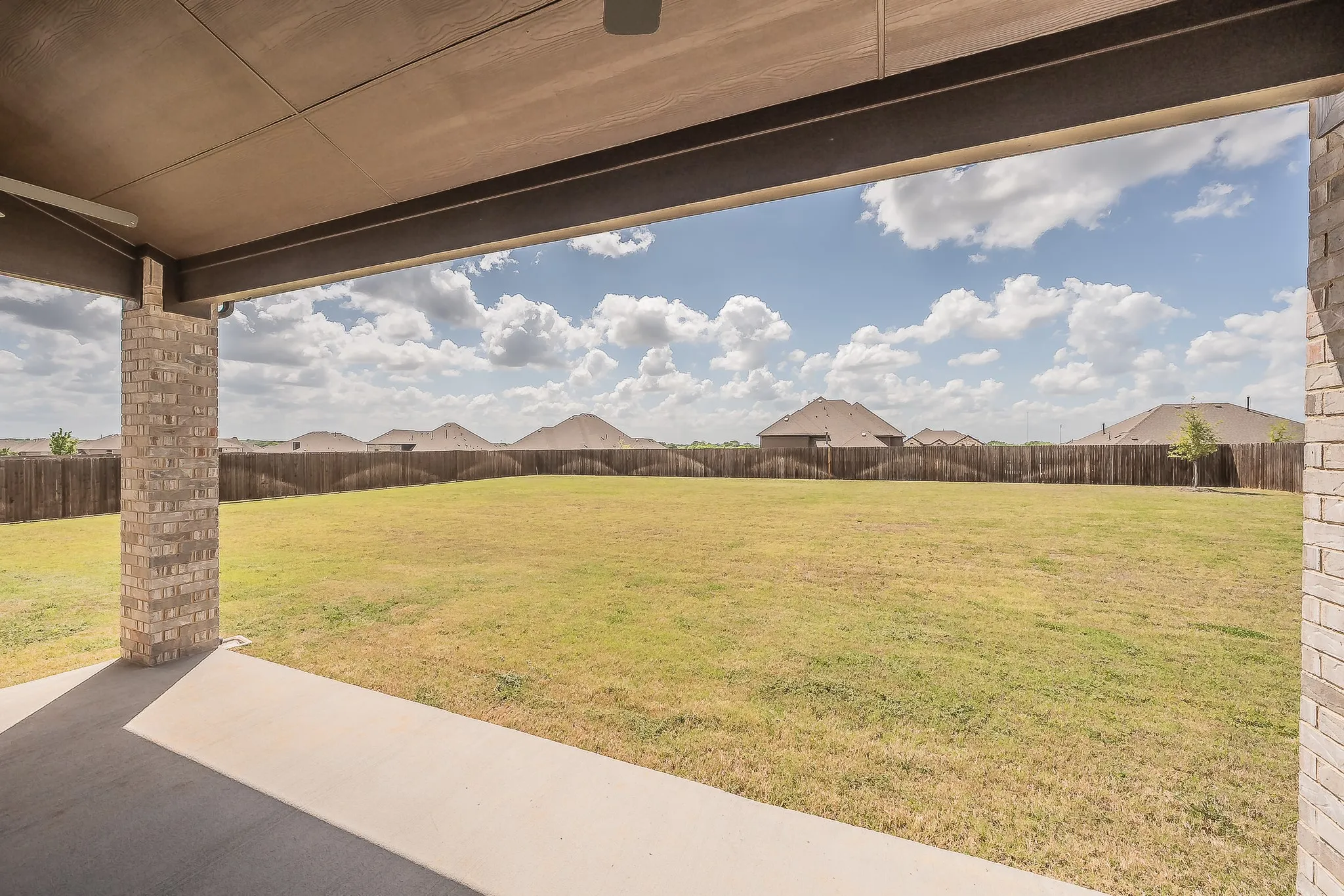 The property features an expansive green lawn, a covered patio with brick columns, and a wooden fence enclosing the yard, sits on 1/2 acre