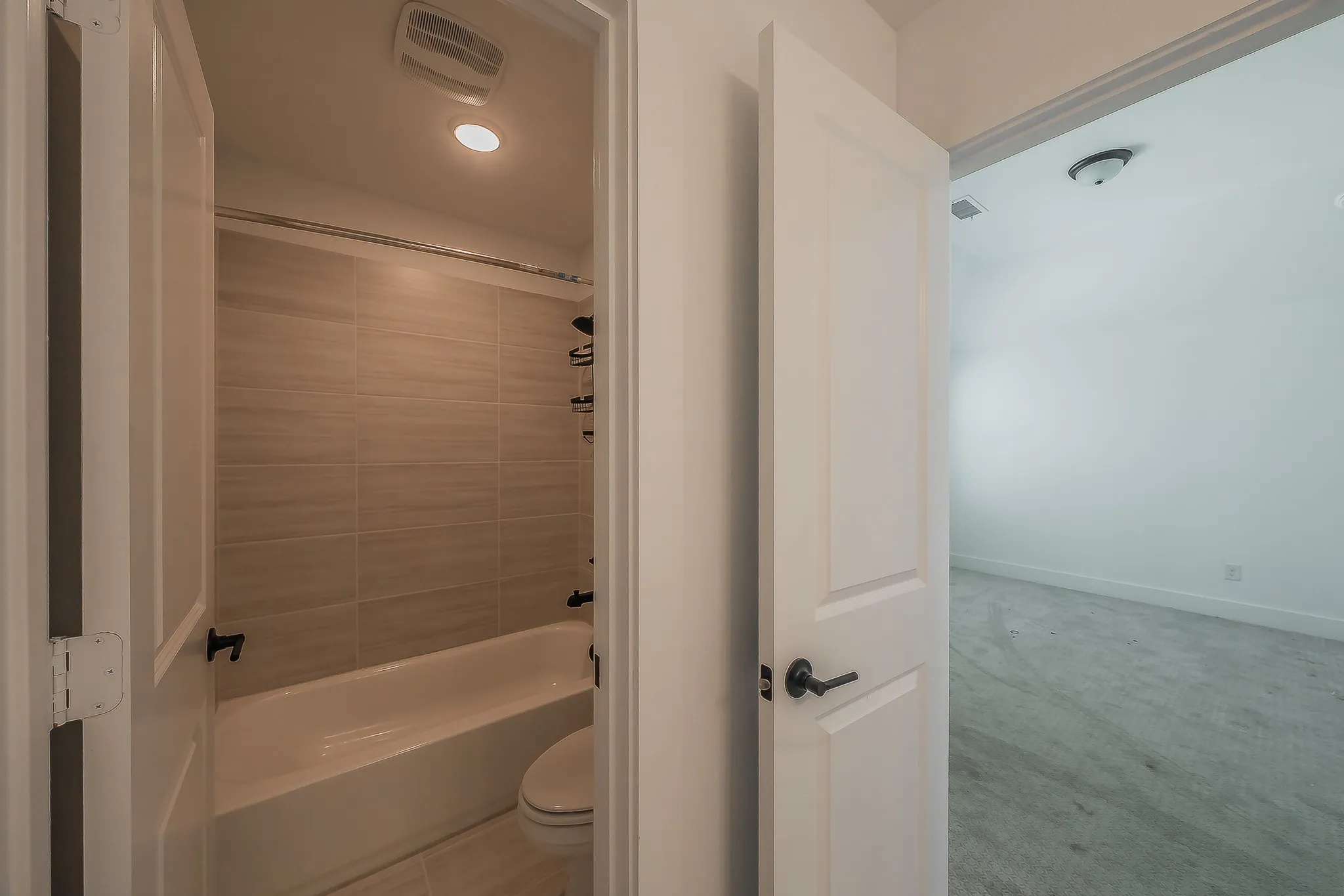 Bathroom with a white tub-shower combination, light-toned horizontal tile surround, and matte black fixtures