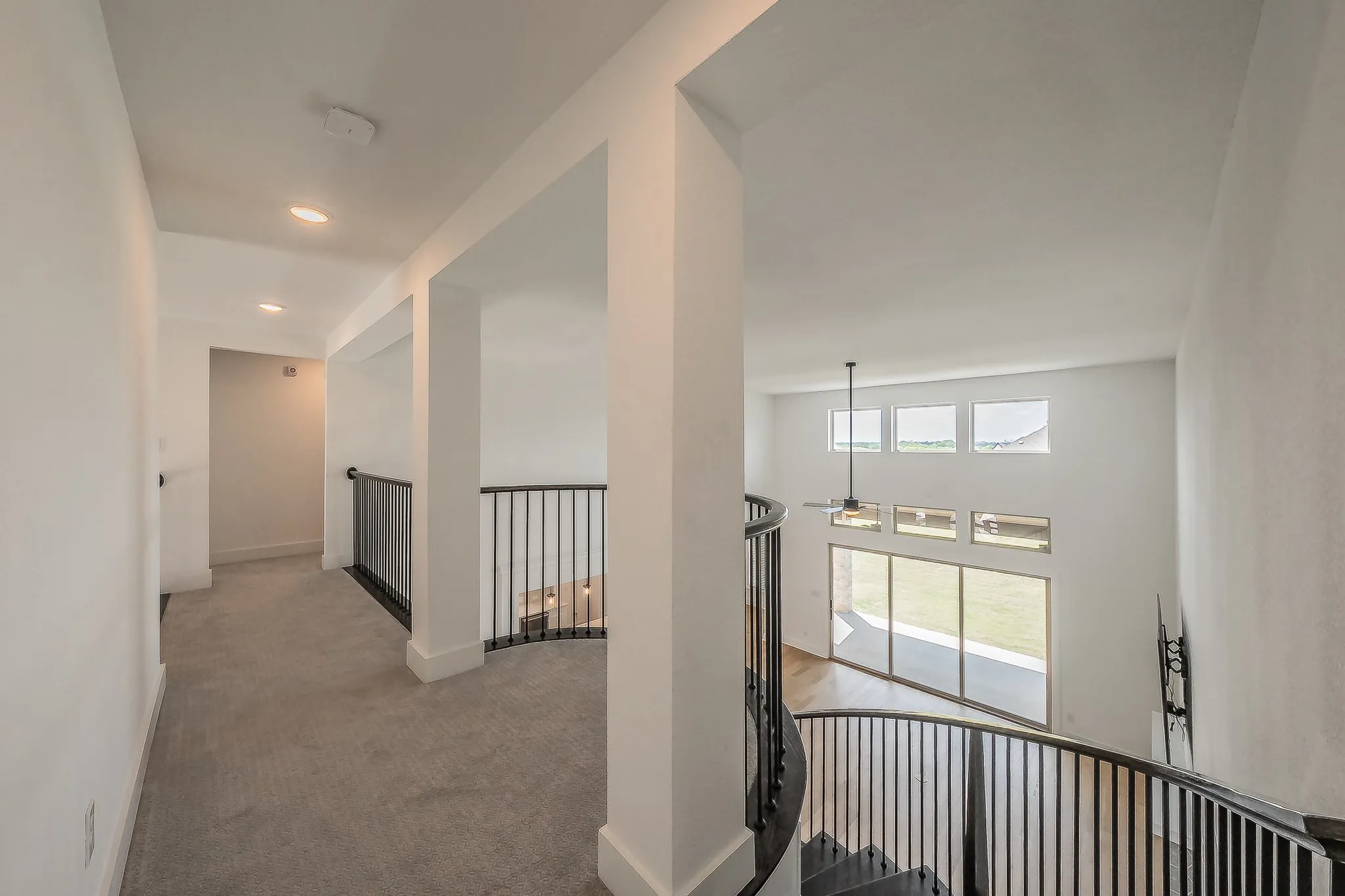 A bright interior with white walls, recessed lighting, and a sweeping curved staircase with black metal railings