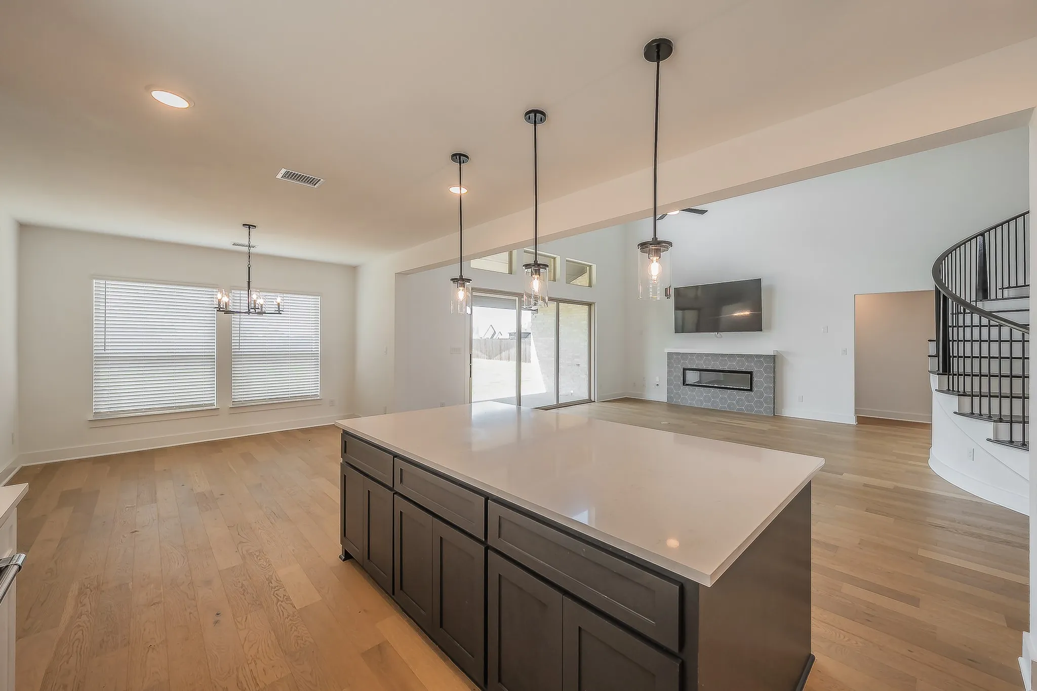Open concept living space featuring light hardwood flooring, a kitchen island with a white countertop and dark cabinetry, and pendant lighting