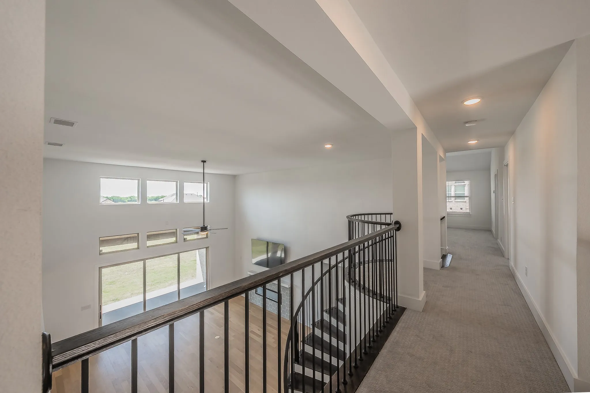 Open loft area featuring a wrought iron railing, light wood-finish flooring, and a contemporary ceiling fan