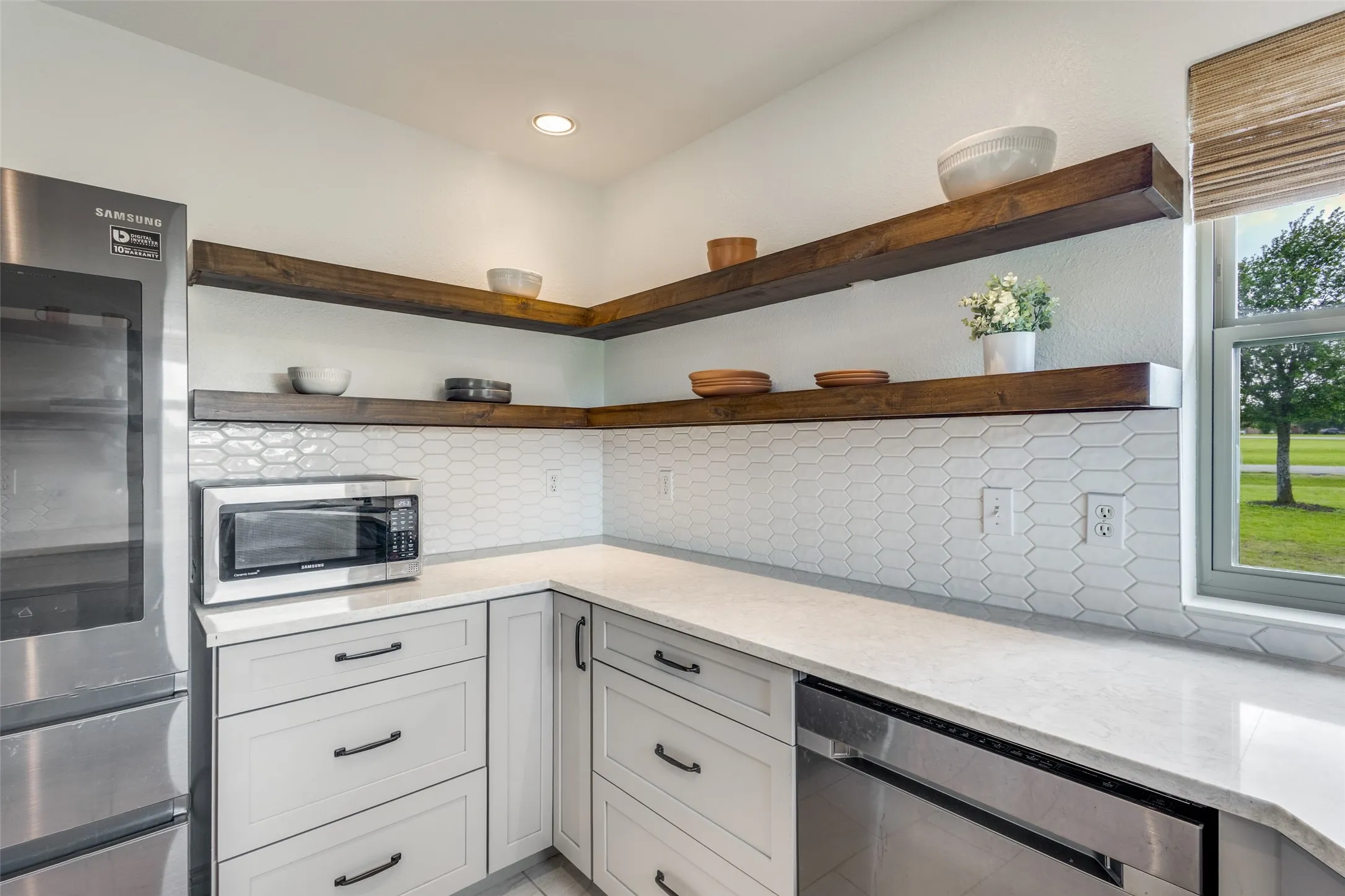 The kitchen features light-toned cabinetry, stainless steel appliances, open wooden shelving, and a patterned tile backsplash