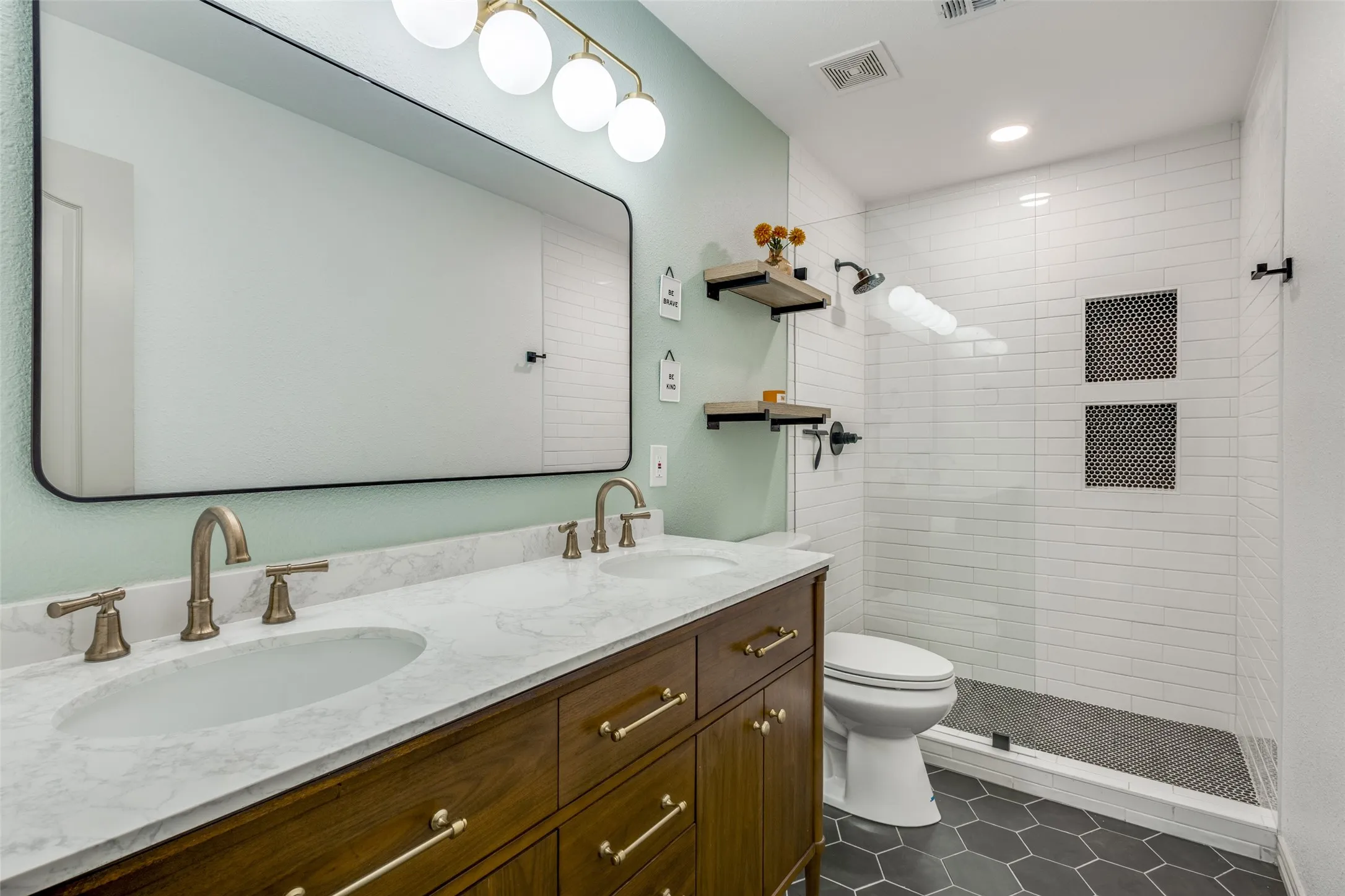 This bathroom features a double vanity with a marble-style countertop, a large mirror, and contemporary light fixtures