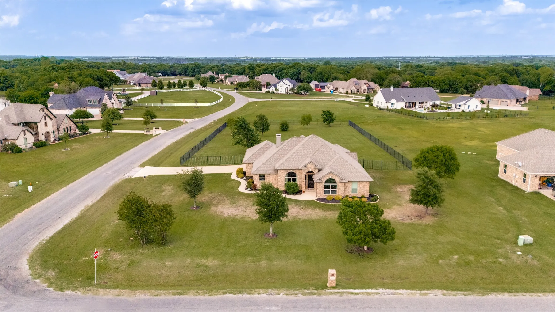 The property is set on an expansive green lawn, featuring an asphalt driveway and a fenced backyard