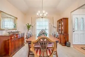 This room features a vaulted ceiling with a chandelier, a large window with sheer curtains, and light-colored carpeting