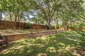 The property features a large grassy yard with mature trees, a wood fence, and a brick retaining wall