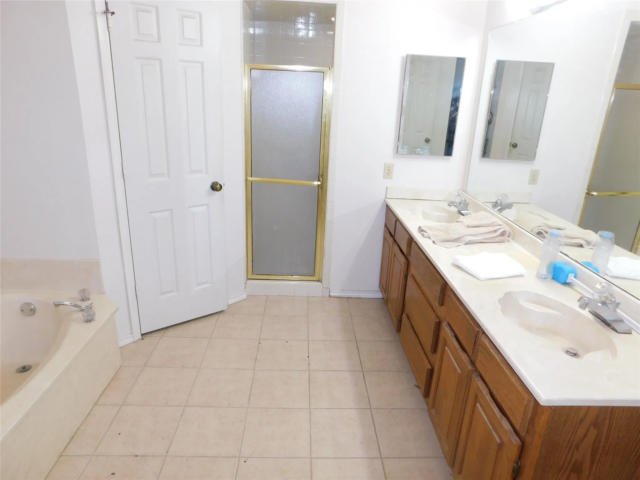 Bathroom featuring tile flooring, a built-in bathtub, a shower with a frosted glass door, and a vanity with two sinks and a mirror