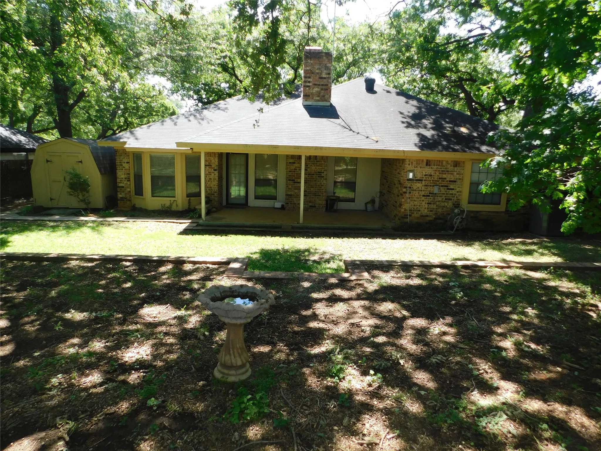 The property features a spacious backyard with a lawn area, mature trees, a brick exterior, and a covered patio