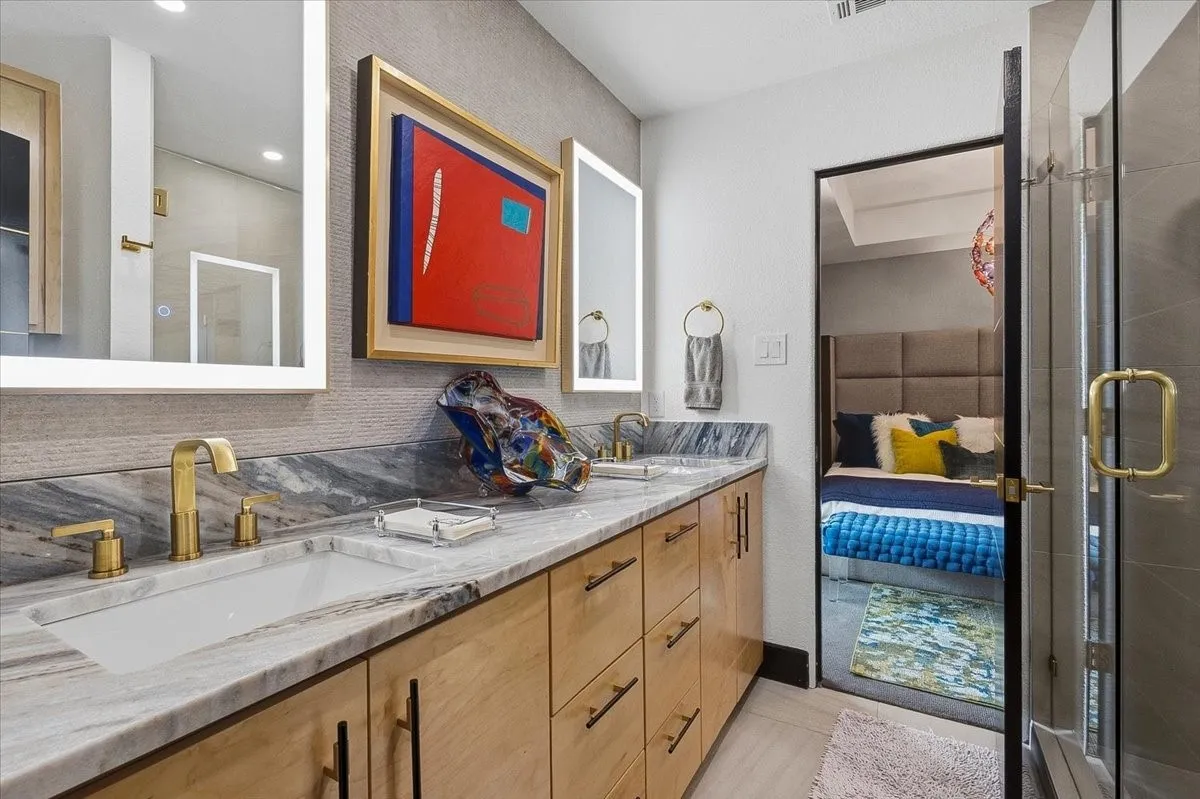 Jack & Jill  bathroom features a double vanity with a marble countertop, undermount sinks, and gold-toned fixtures