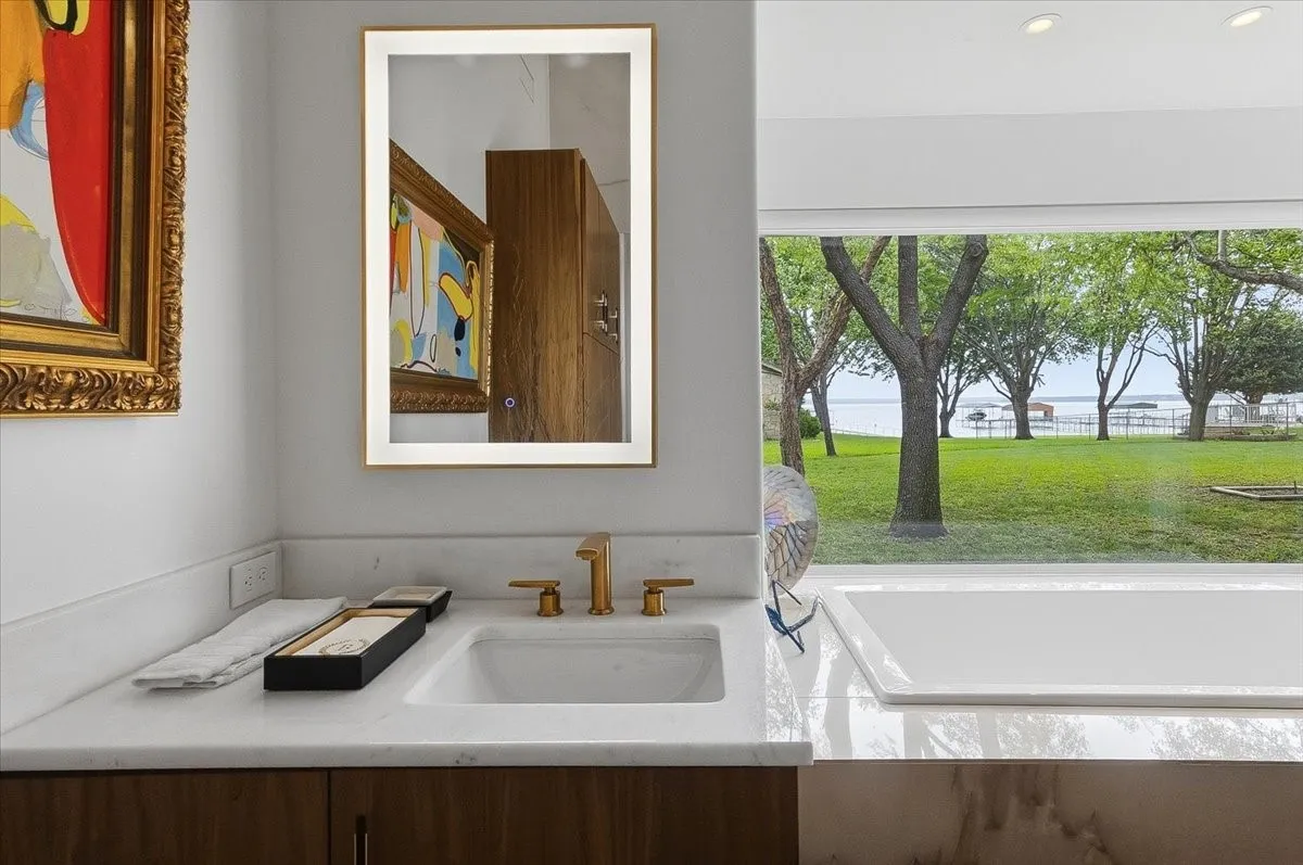 Double Vanities with white countertops and a golden faucet, featuring a large window providing views of a grassy area and the lake