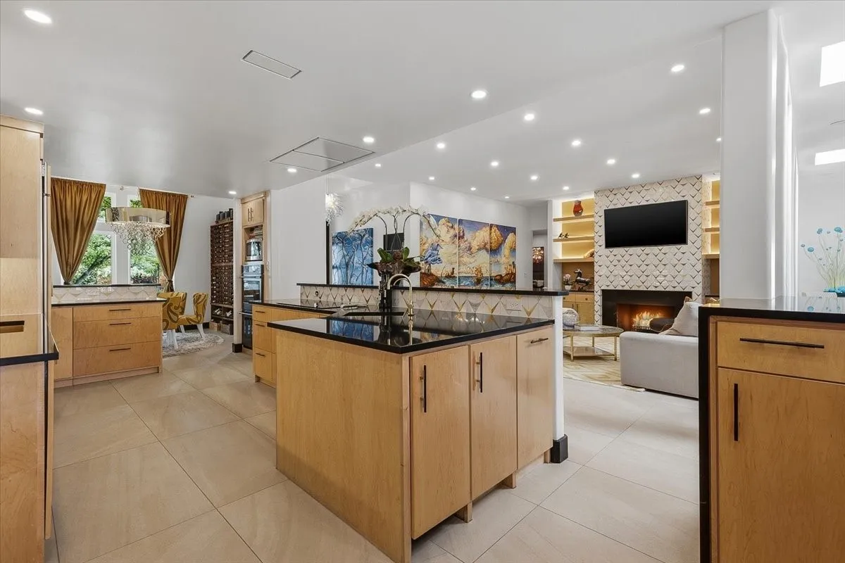  The kitchen features light wood cabinetry, black countertops, and a central island with a sink