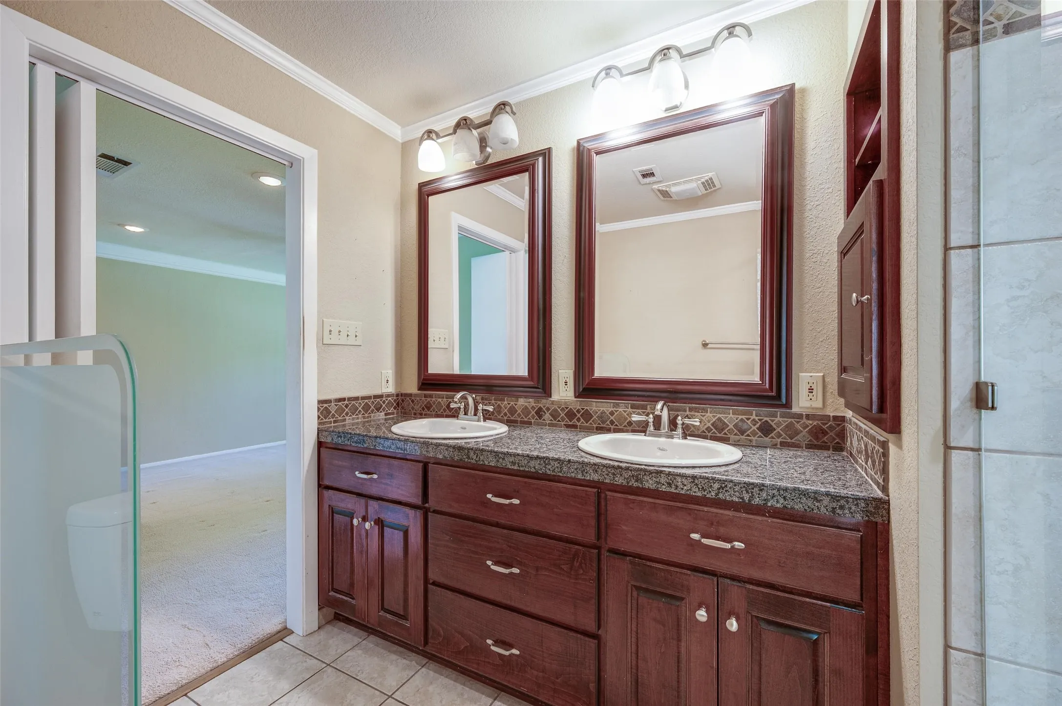 Granite counters, rich wood cabinetry, stainless fixtures, and dual framed mirrors in primary bathroom.
