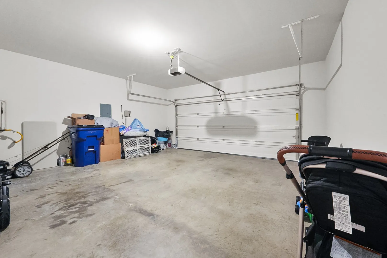 Spacious garage with a sectional overhead door, exposed garage door opener, and a light-colored concrete floor