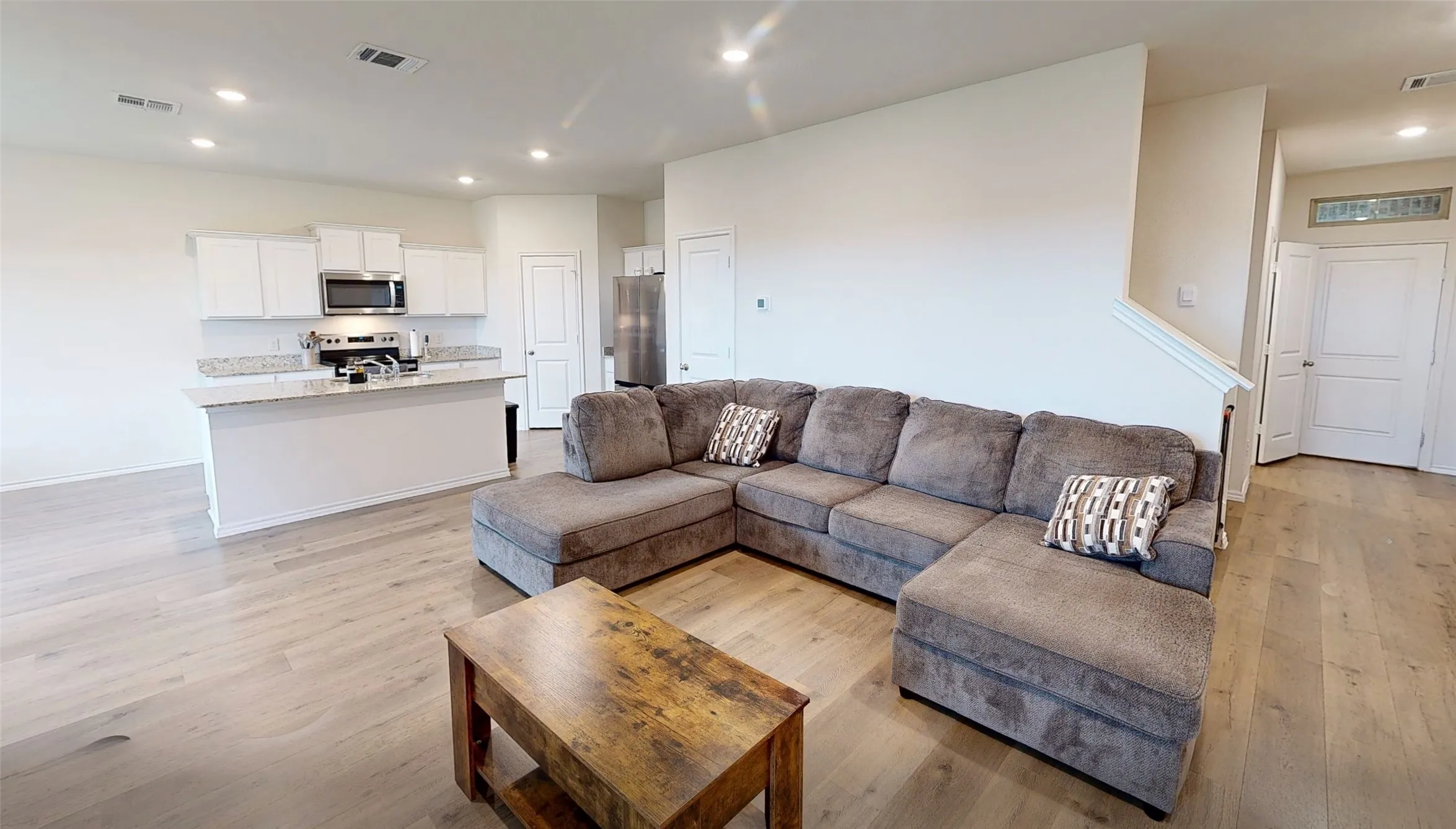 Open-concept living space featuring wood-finish flooring, recessed lighting, and a white kitchen with stainless steel appliances