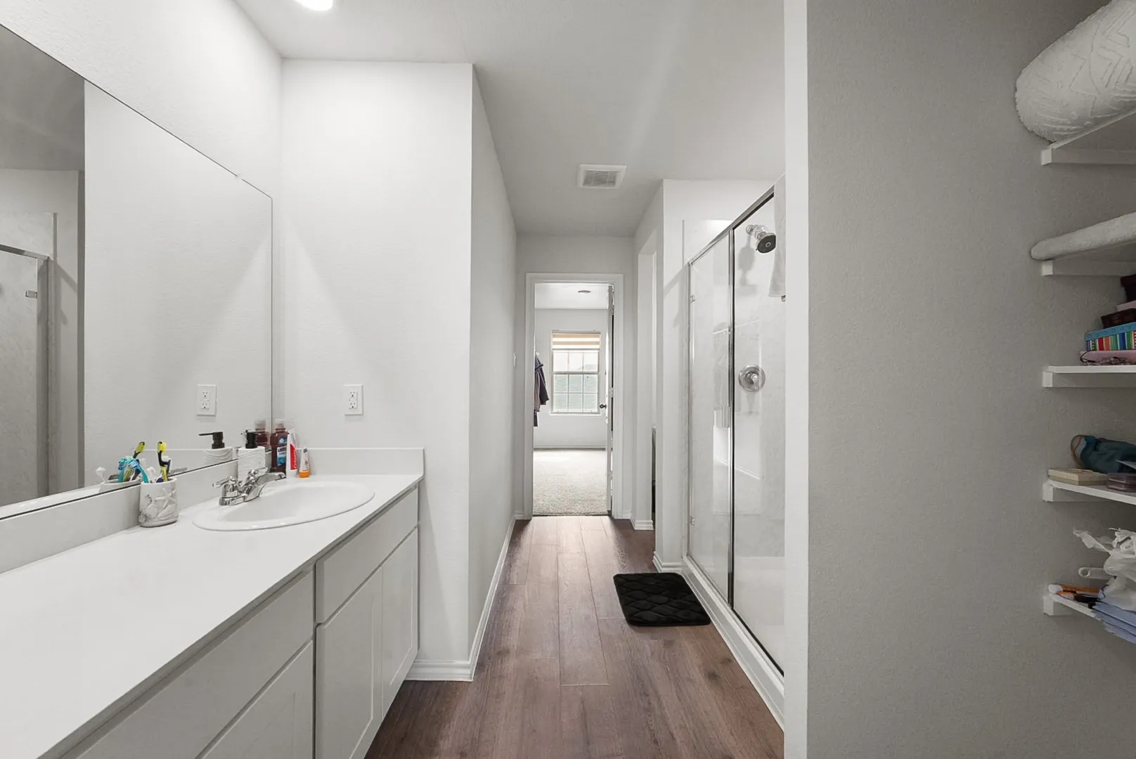 Bathroom featuring a single vanity with an integrated sink, a glass-enclosed shower, wood-finish flooring, and built-in shelving