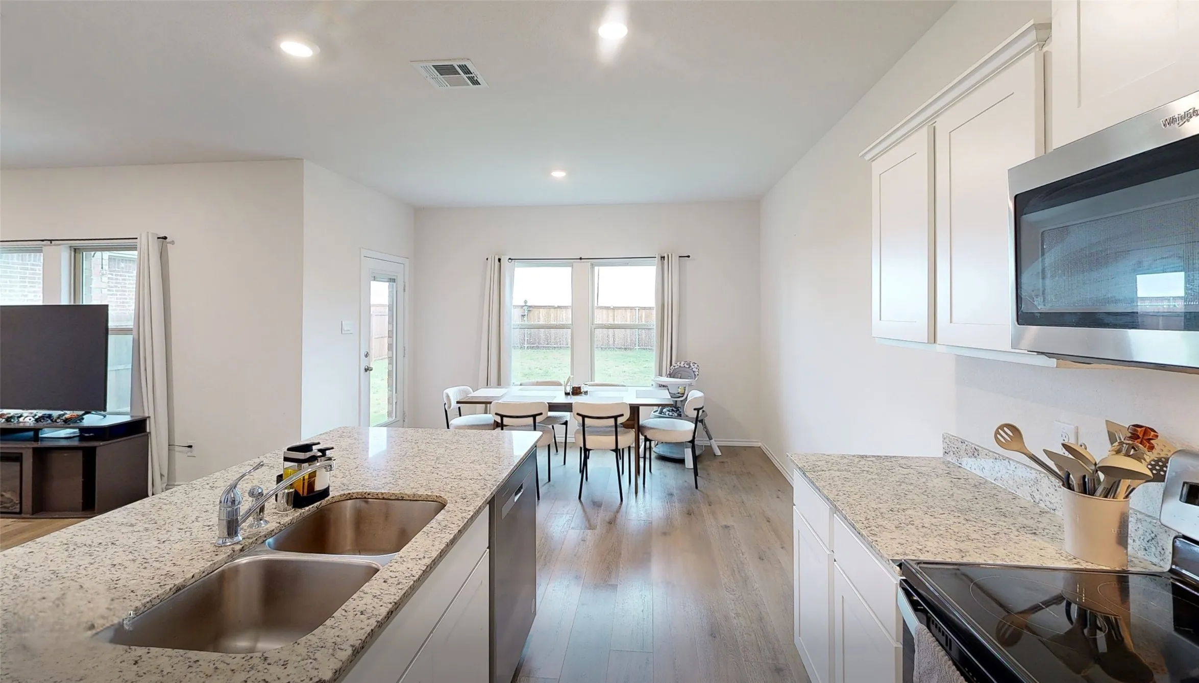 Open-concept kitchen and dining area featuring granite countertops, wood-finish flooring, white cabinetry, and stainless steel appliances