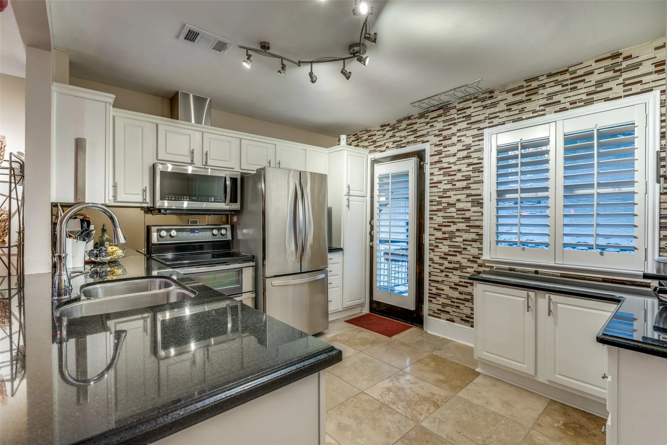 Kitchen with appliances with stainless steel finishes, dark stone counters, white cabinetry, and sink