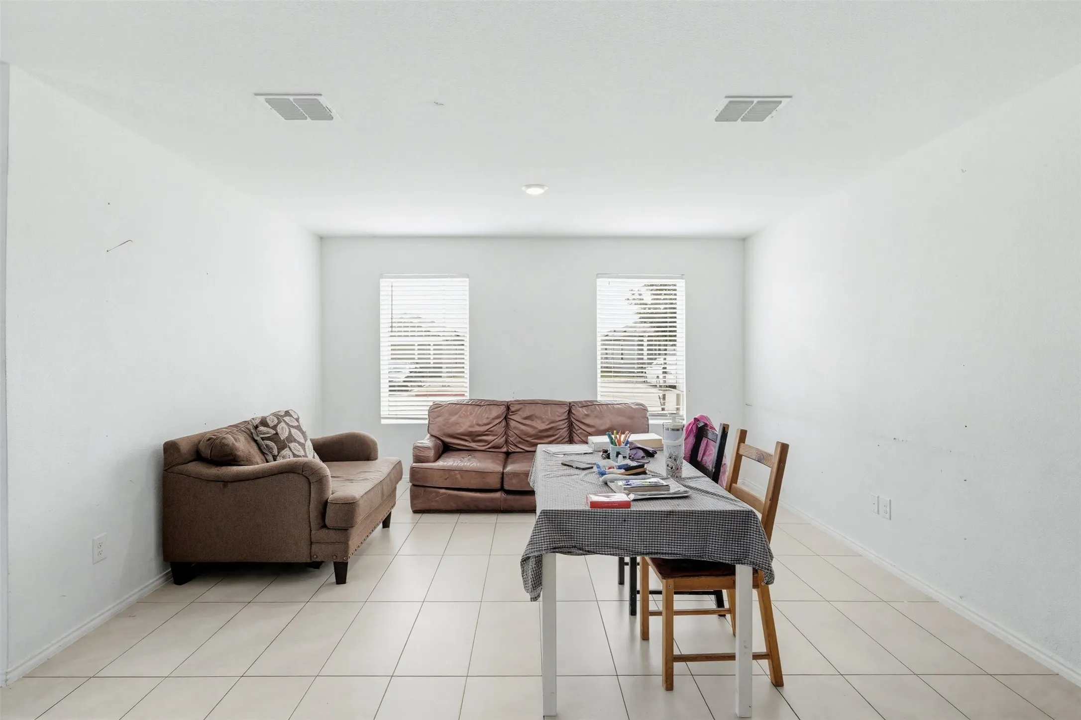 Spacious room featuring light-colored tile flooring, white walls, and two windows with blinds
