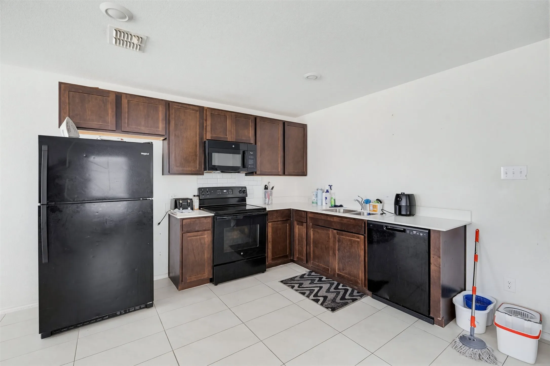 The kitchen features dark wood cabinetry, white countertops, and white tiled flooring
