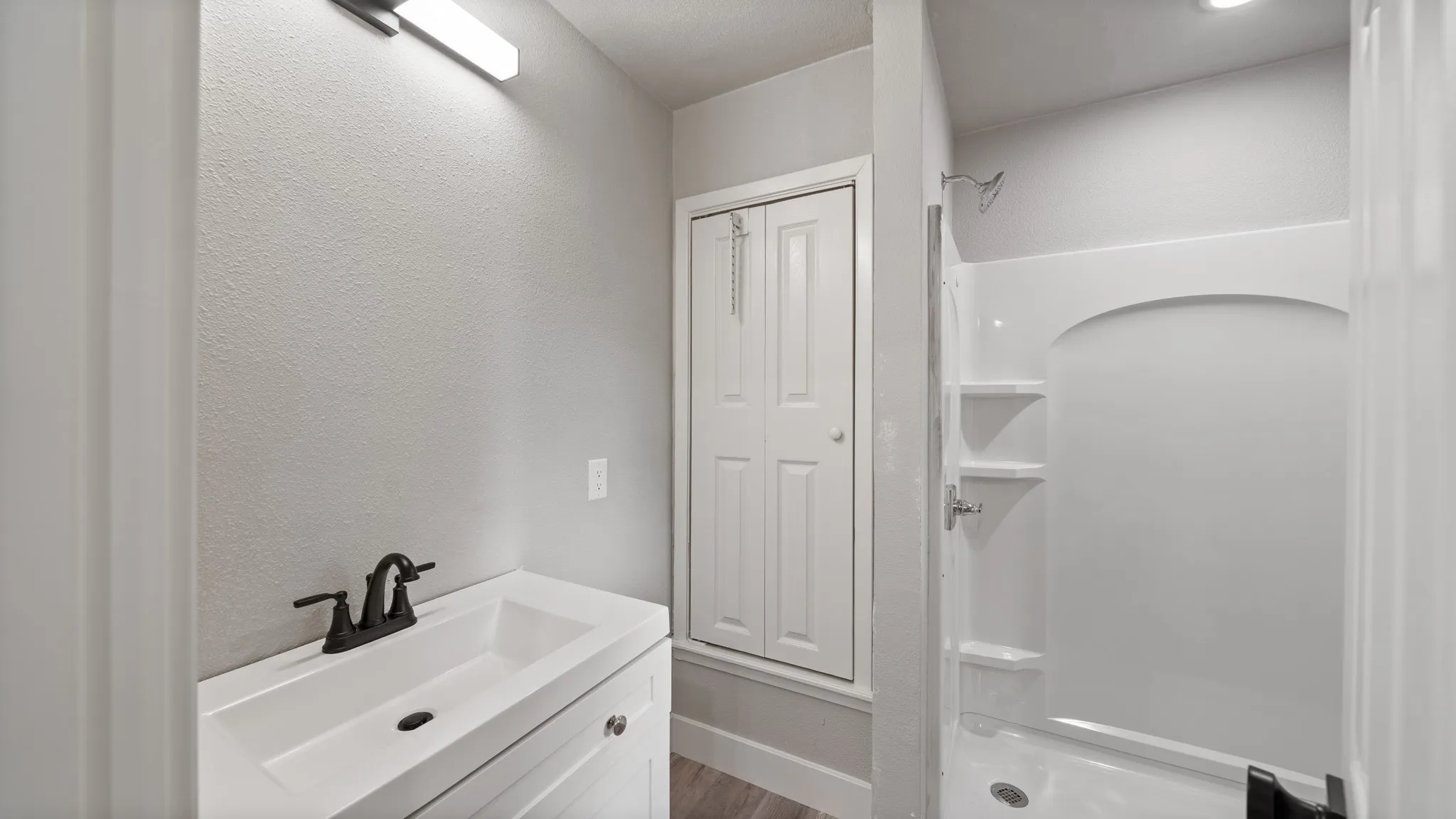 This bathroom features a vanity with a white sink and dark-toned faucet, a light fixture above the vanity, and a shower with built-in shelving