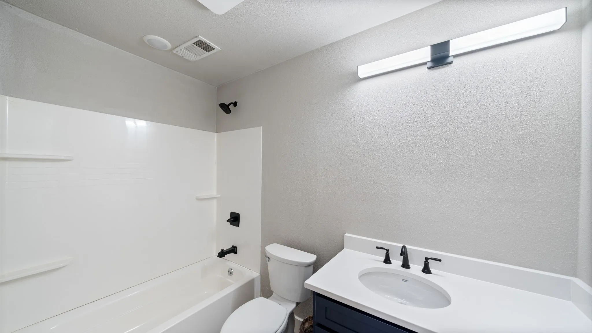 The bathroom features a white bathtub with a shower, a vanity with a white countertop and sink, and a toilet