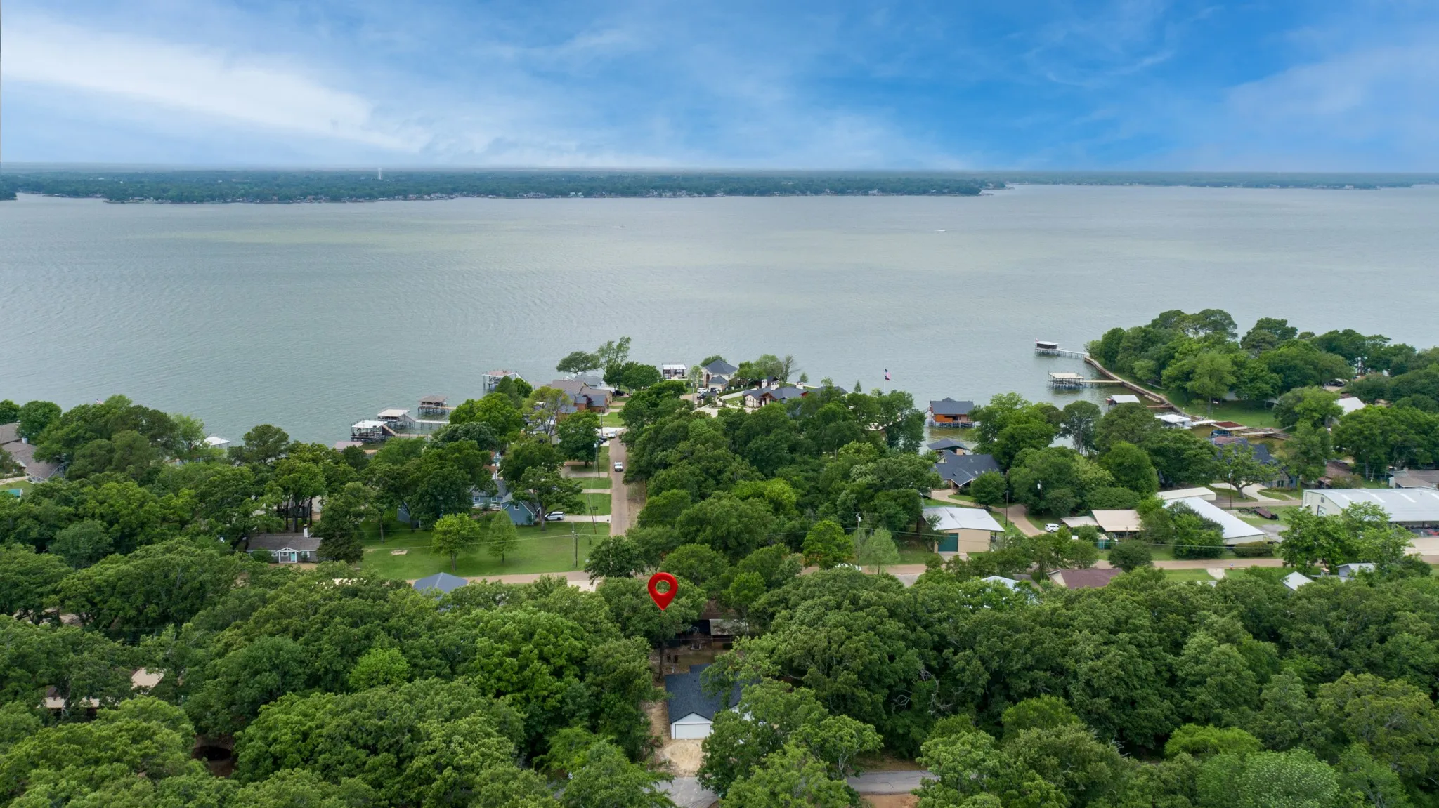 Aerial view showcasing the property's location within a lush, tree-filled neighborhood, with a large body of water visible in the background and properties with private docks along the shoreline