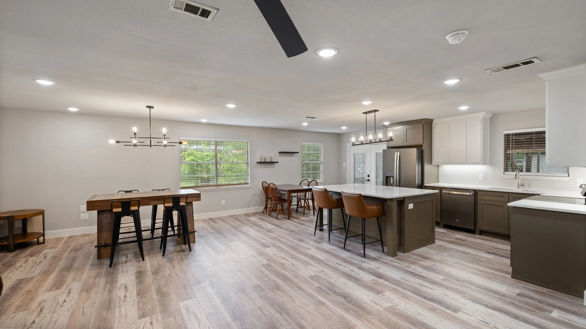The kitchen and dining area features recessed lighting, a large island with seating, stainless steel appliances, and wood-look flooring