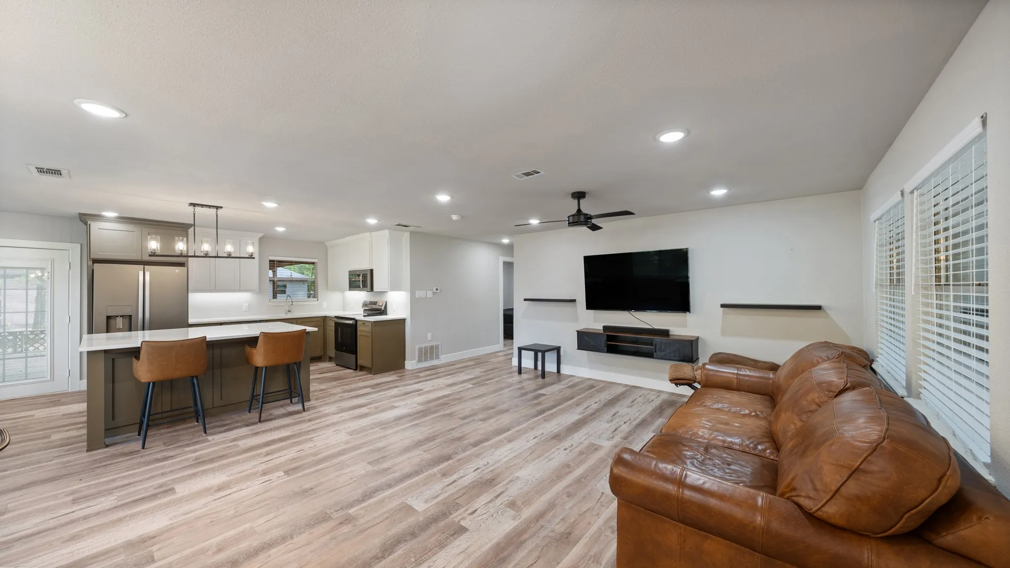 The open concept living area features recessed lighting, light-toned flooring, and windows with blinds, providing natural light