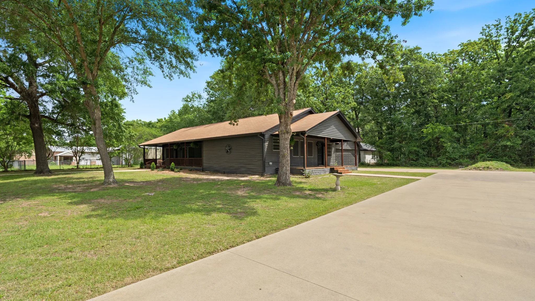 The property features a dark-colored exterior with a front porch, a well-maintained lawn with mature trees, and a concrete driveway