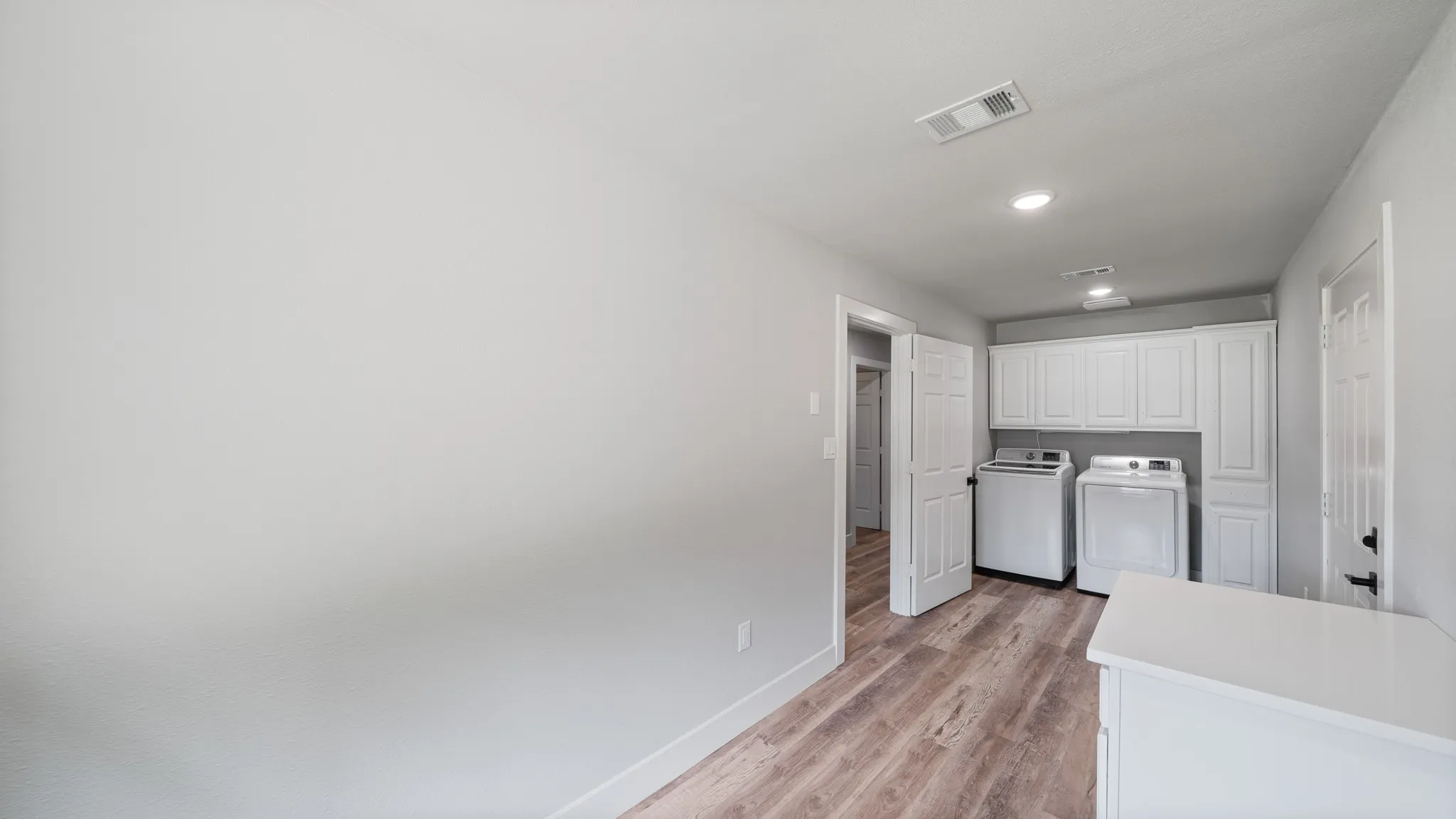 Laundry area featuring wood-look flooring, white cabinetry, recessed lighting, and a white countertop