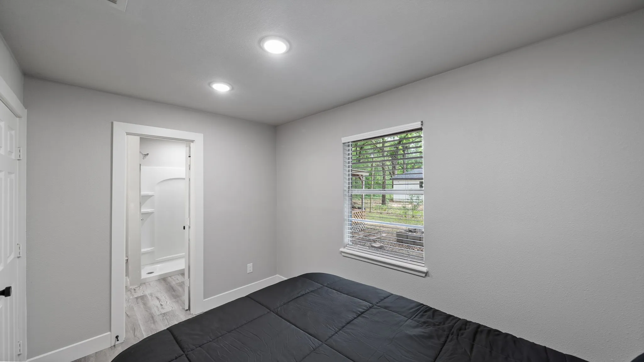 Bedroom with recessed lighting, light gray walls, and a window with blinds overlooking greenery