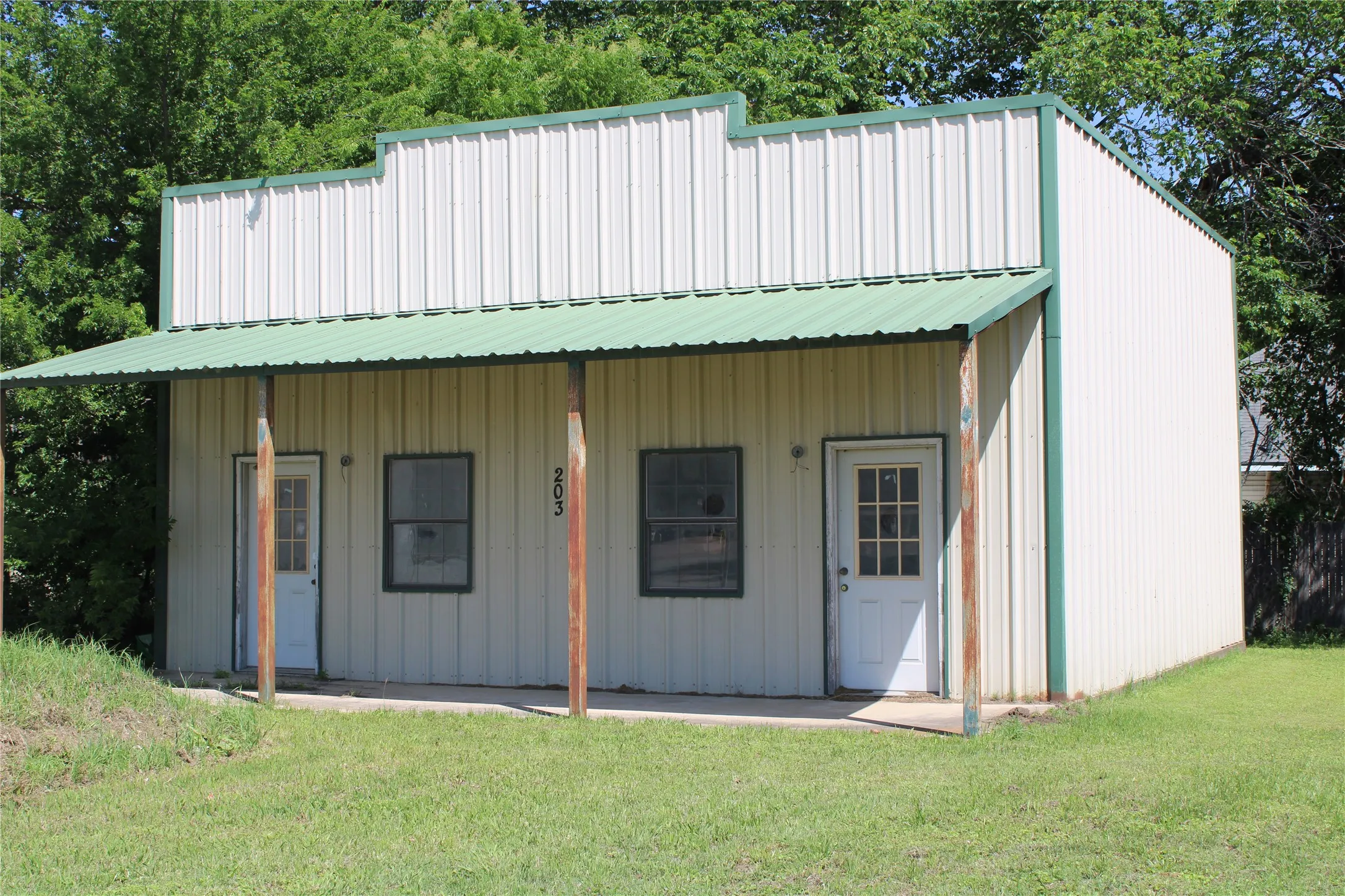 The property features a metal siding exterior with a green roof, a covered porch supported by columns, and two entry doors