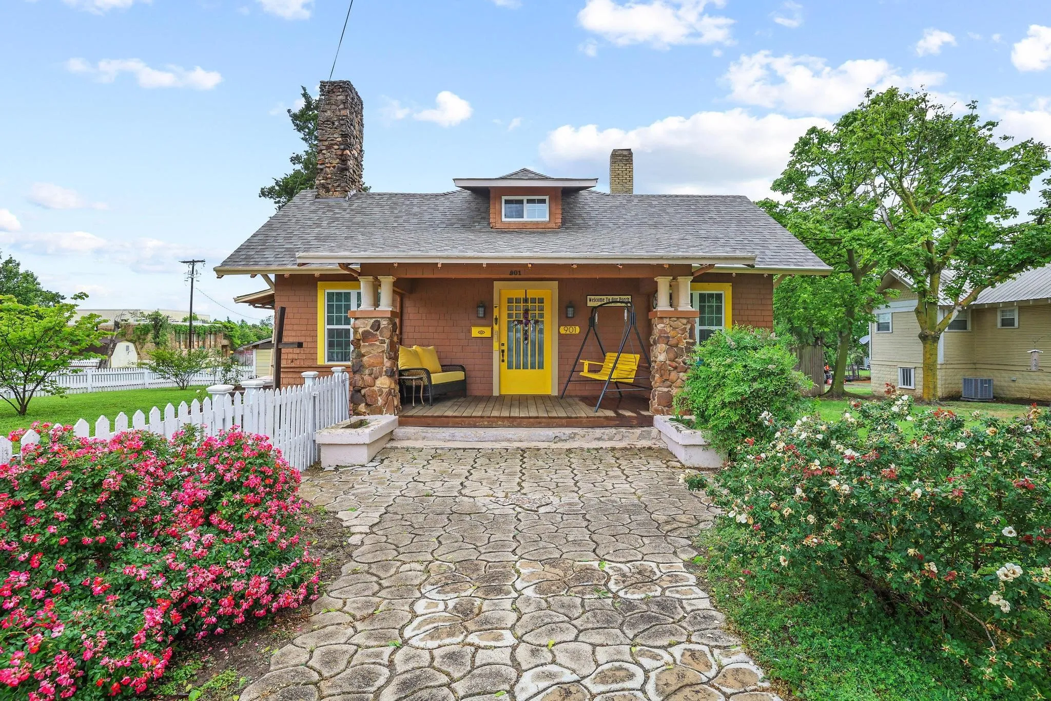 The property features a charming front porch with stone pillars, a bright yellow front door, and a patterned stone pathway leading to the entrance