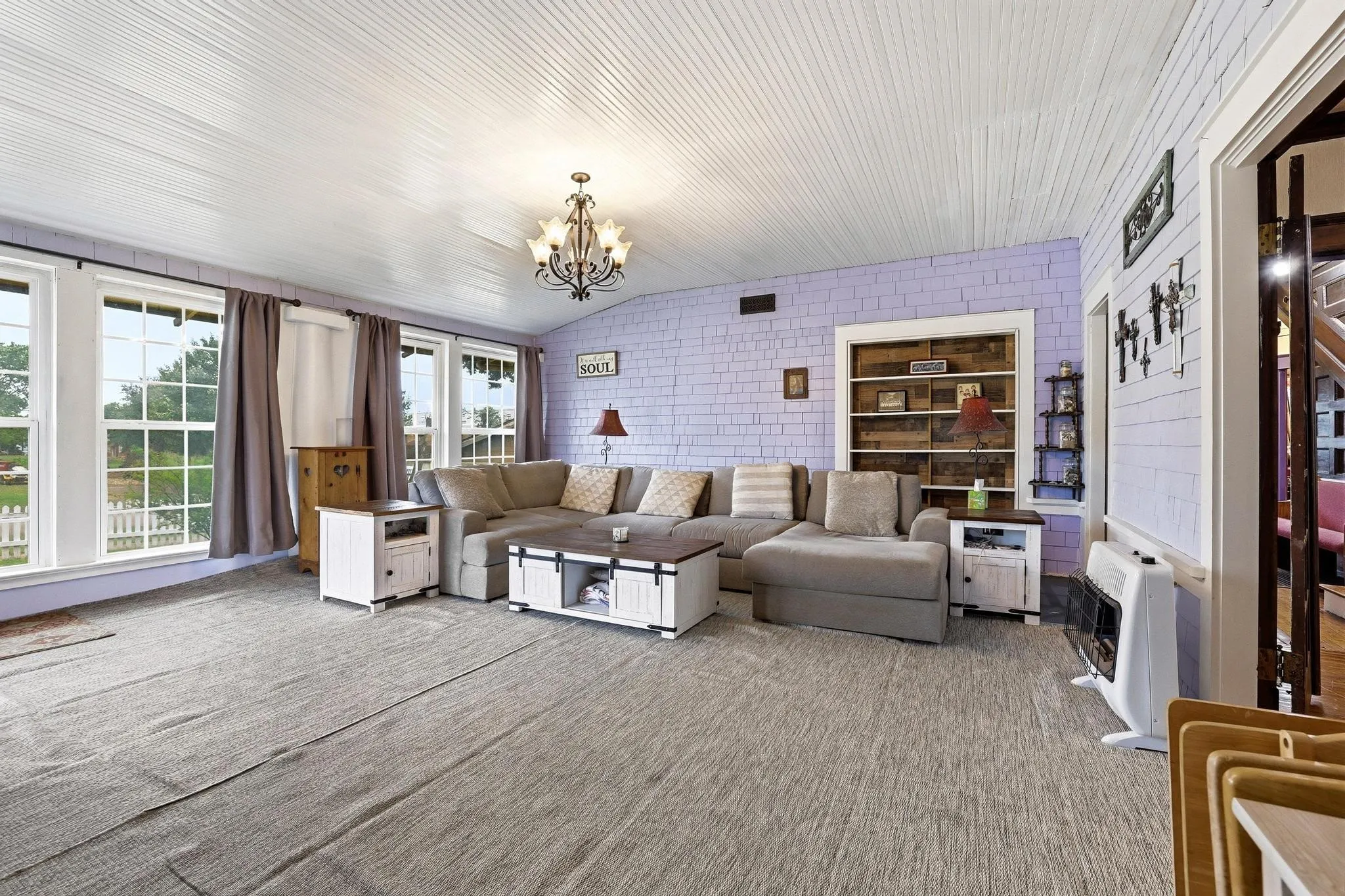 Spacious living area featuring a light-colored ceiling with horizontal paneling, wide plank flooring, and a built-in bookshelf