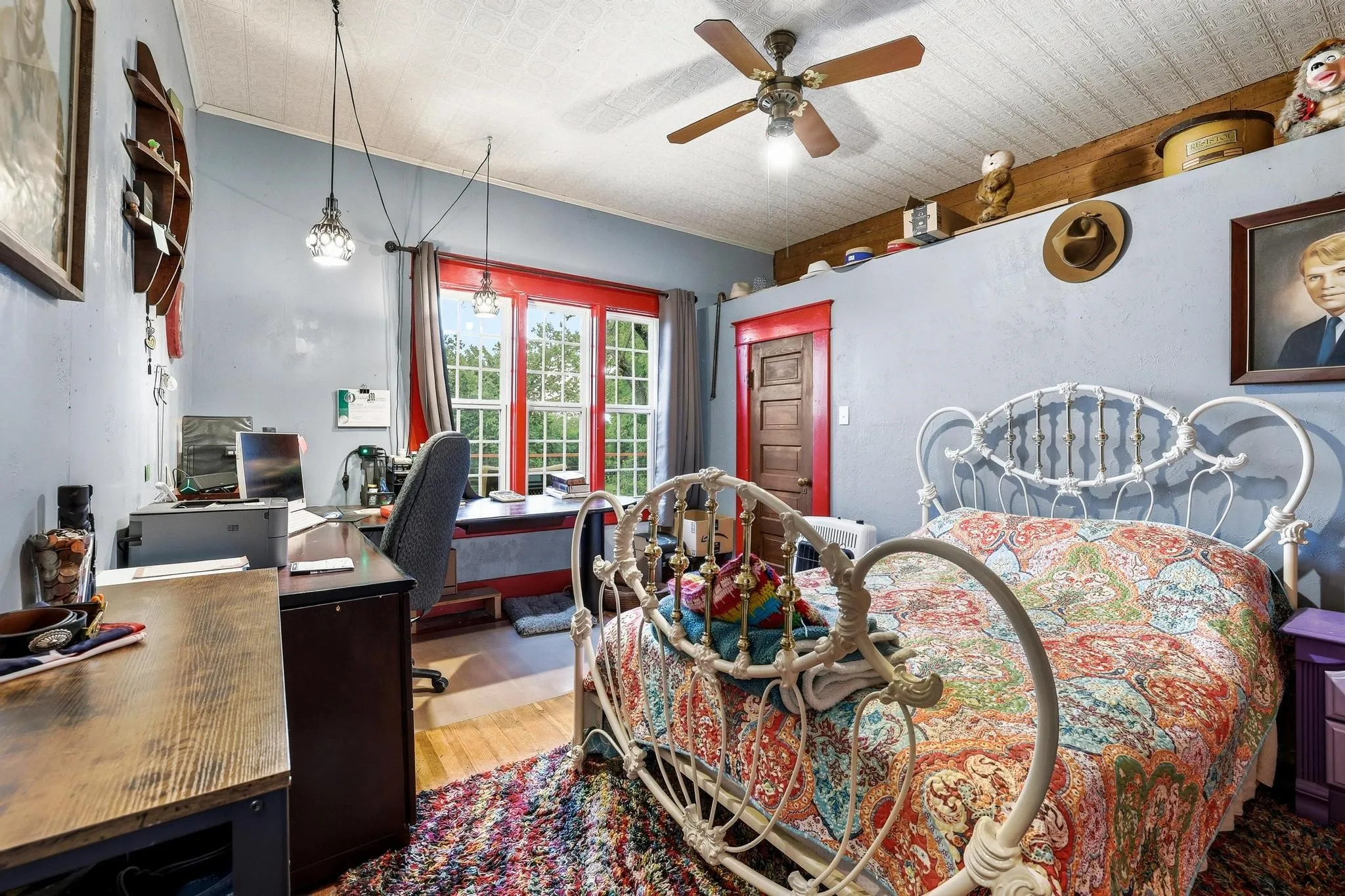 This room features hardwood flooring, a ceiling fan with integrated lighting, and large windows with red trim
