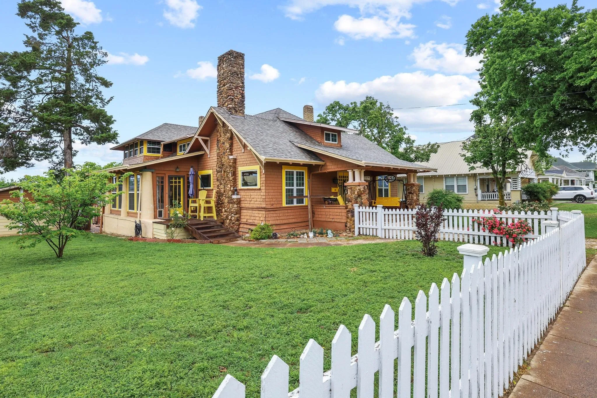 The property features a stone chimney and wood shingle siding, complemented by a white picket fence