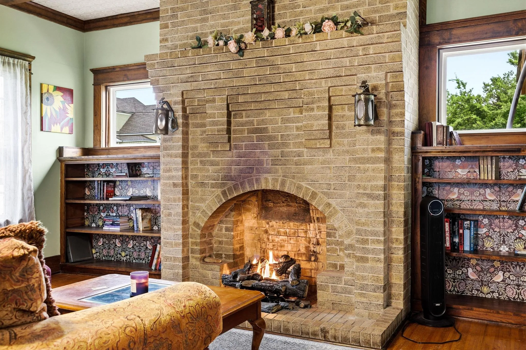 Inviting living area featuring a brick fireplace with an arched firebox, built-in wooden bookshelves, and wooden trim around the windows and ceiling