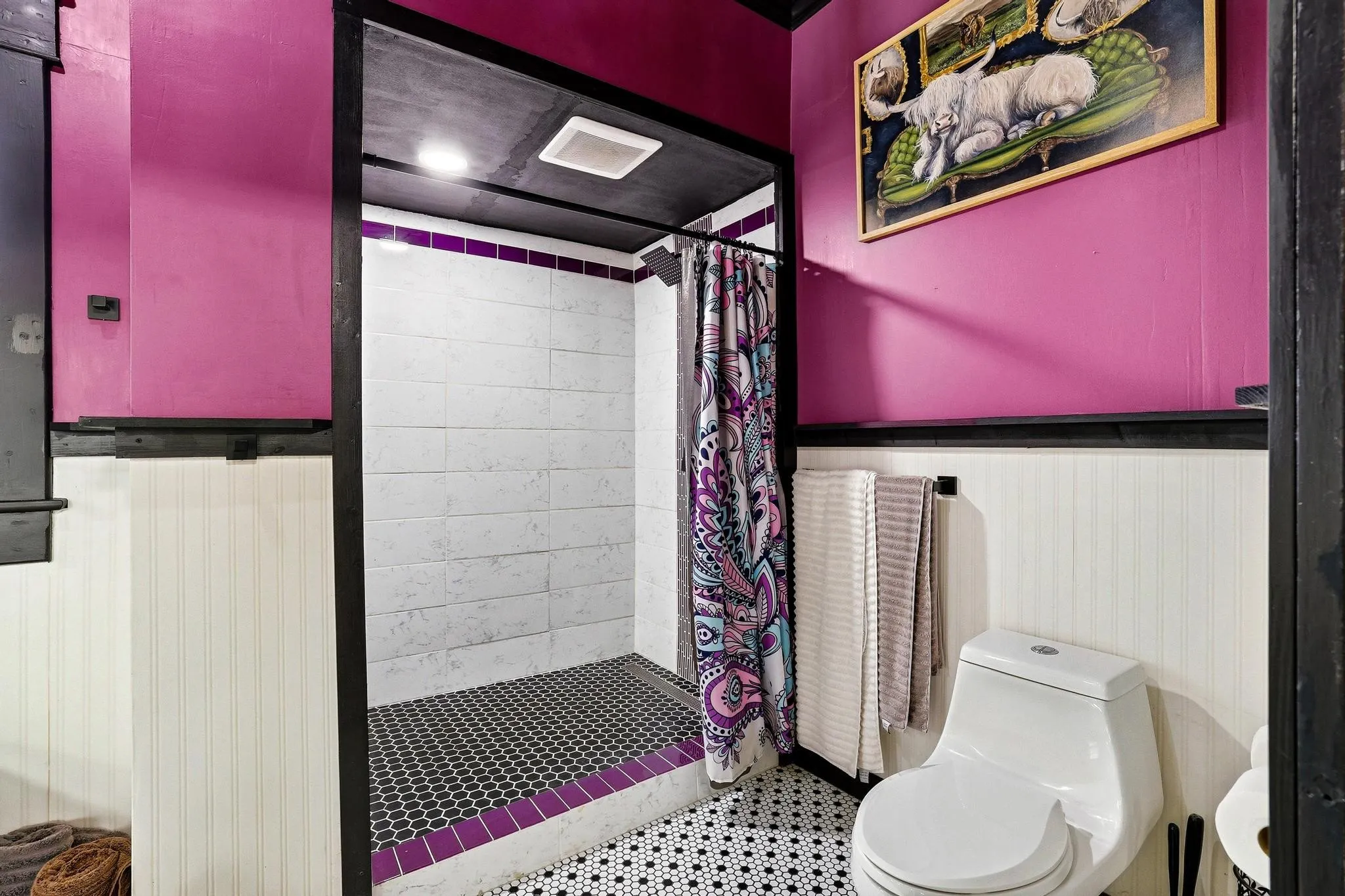Bathroom featuring a shower with white subway tiles and black hexagon floor tiles, white beadboard paneling, and a white toilet