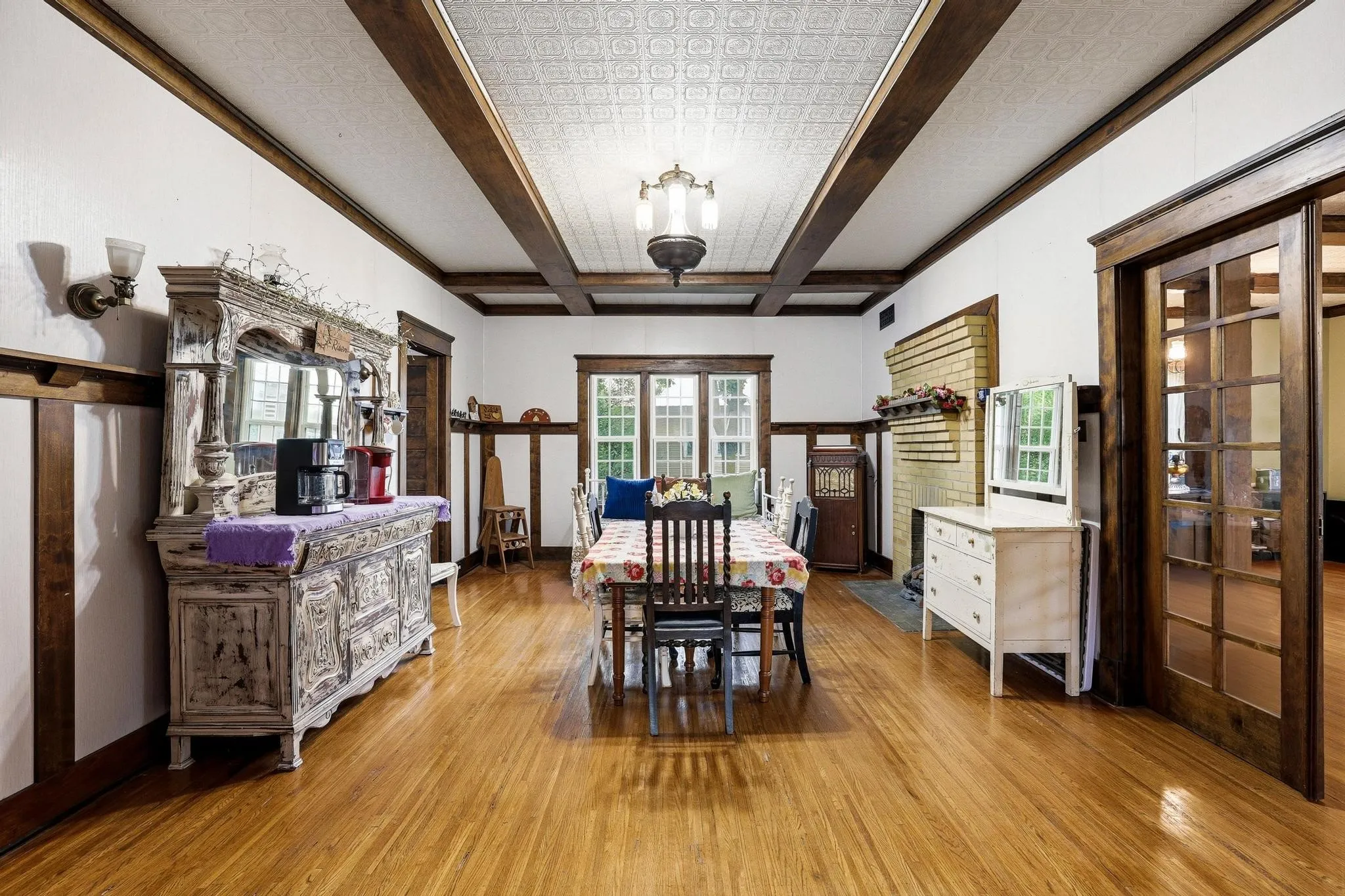 This room features hardwood floors, white walls with dark wood trim, and a patterned ceiling with exposed dark wood beams