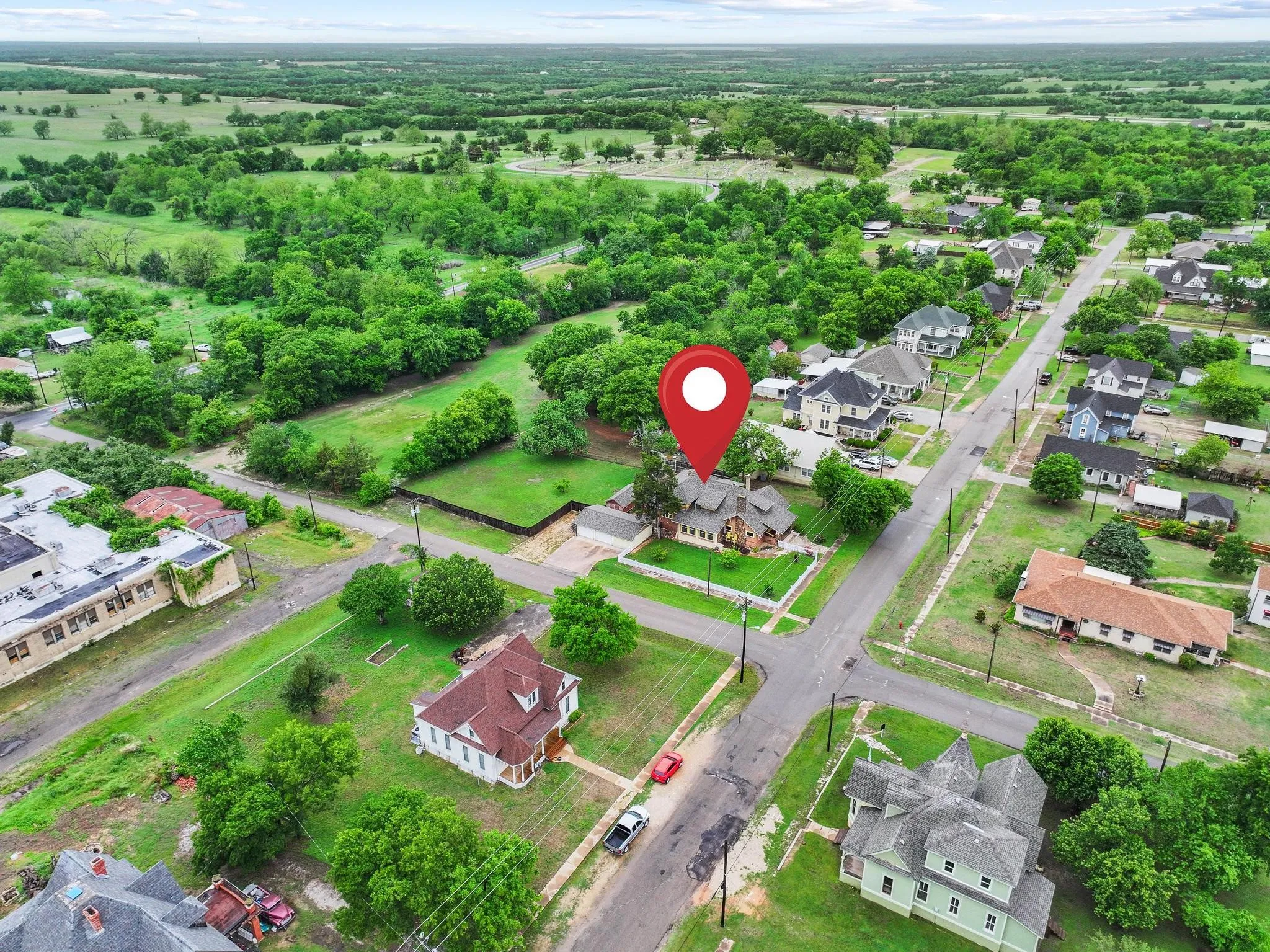 Aerial view showcasing the property situated on a corner lot, surrounded by mature trees and well-maintained green spaces