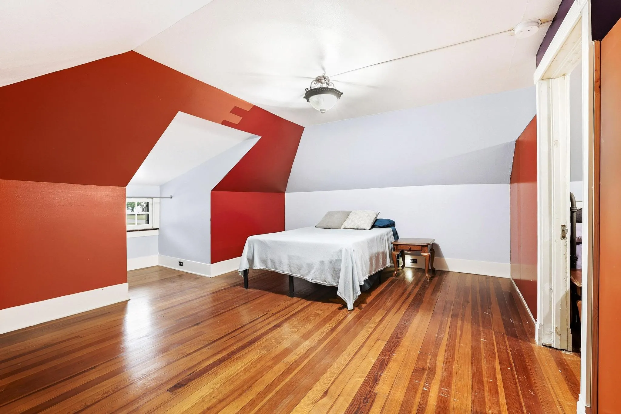 This room features rich hardwood flooring, an angled ceiling, and a window providing natural illumination