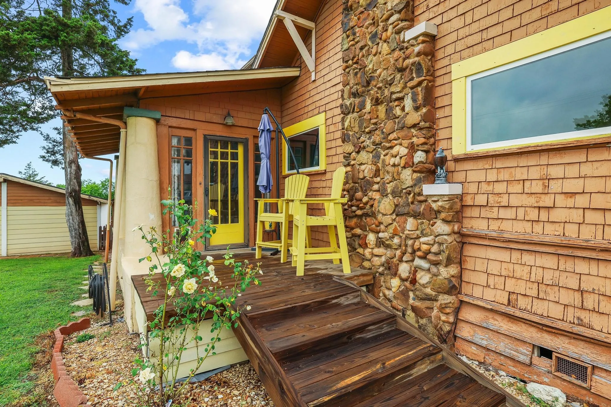 This property features a welcoming deck with wooden stairs, a stone chimney, and shake siding