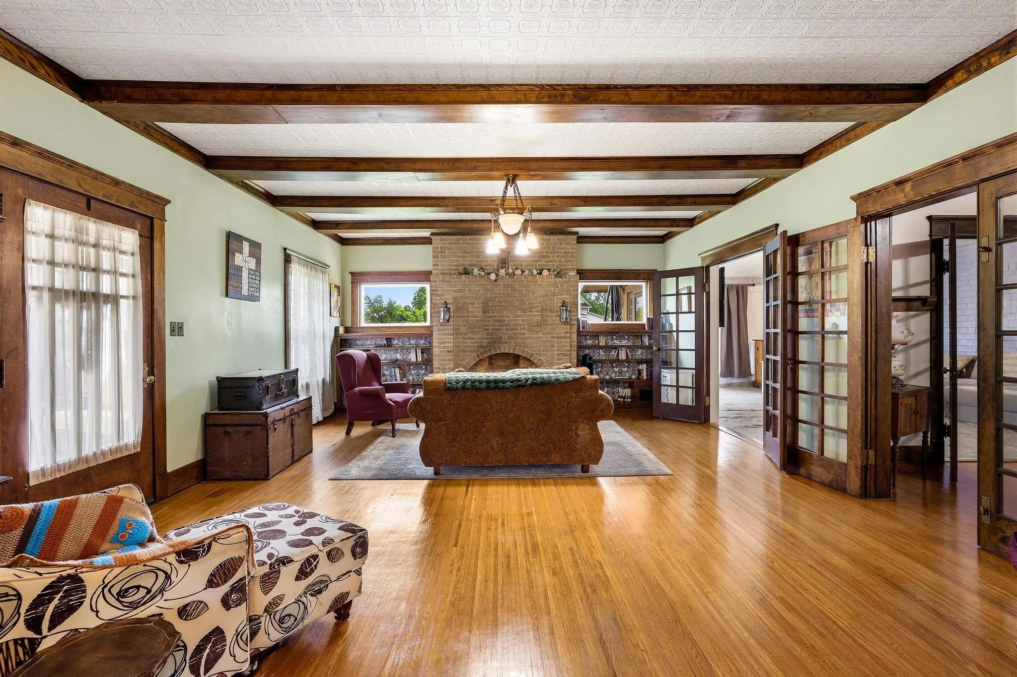 This expansive living area features polished hardwood floors, exposed wood ceiling beams, and a brick fireplace