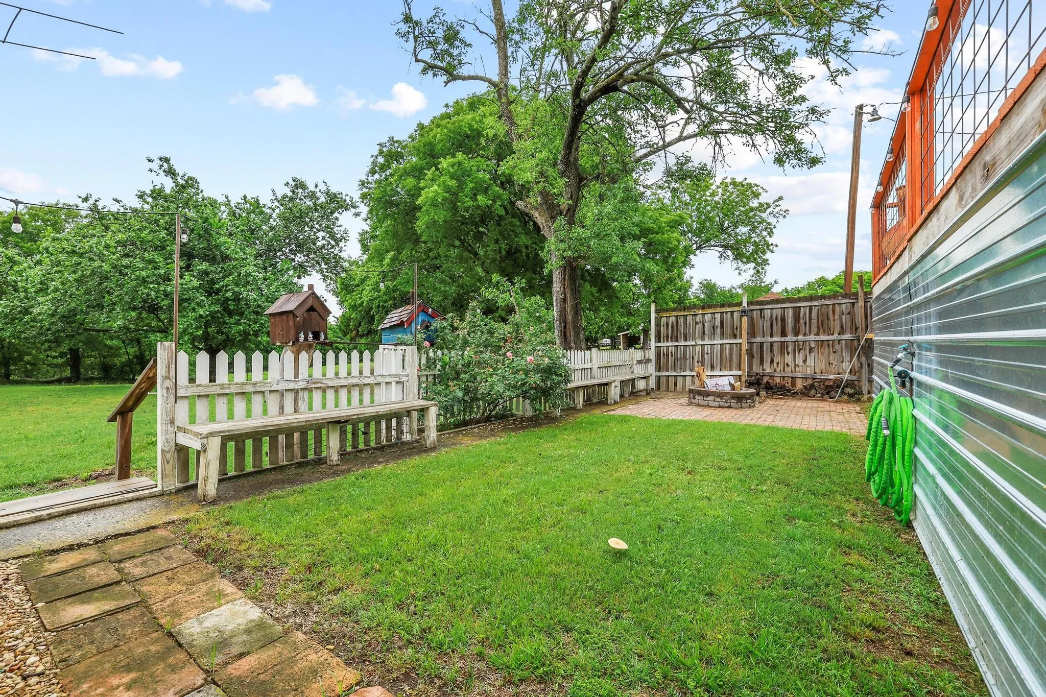 The property features a green lawn area, a brick patio, and a wooden fence and fire pit