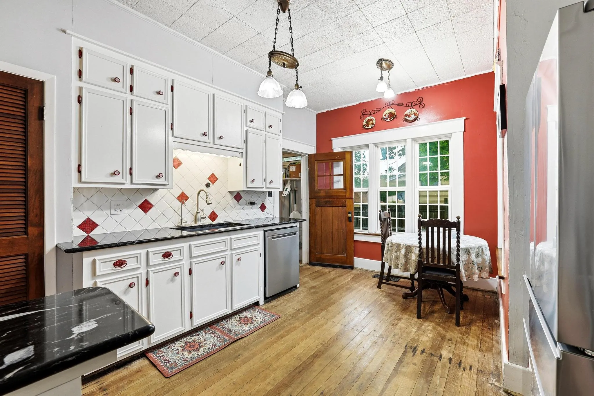 The kitchen features white cabinetry with red hardware, a patterned tile backsplash, and a black countertop