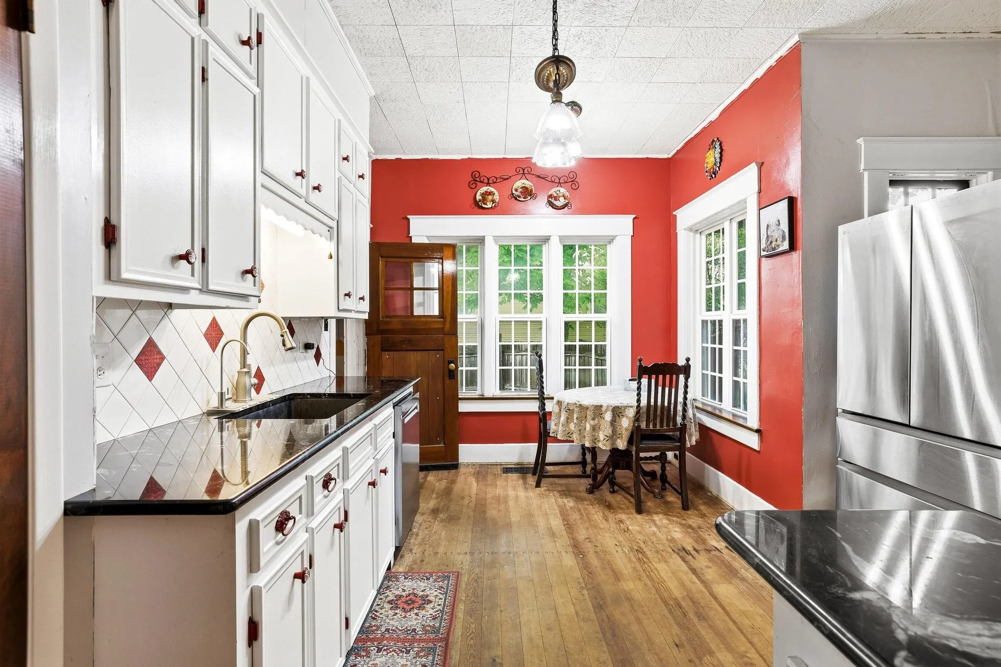Kitchen featuring white cabinetry, black countertops, a tile backsplash with red accents, and stainless steel appliances