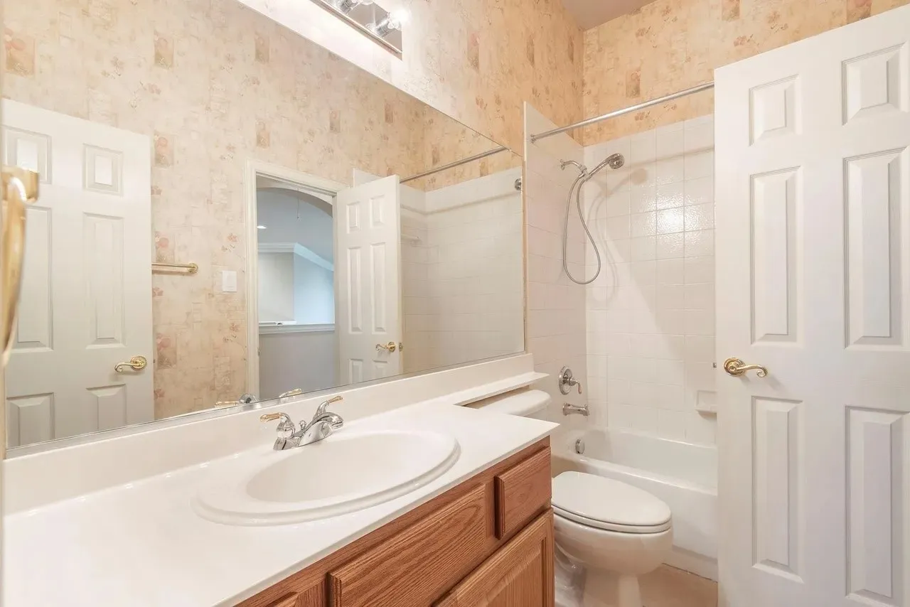 Full bathroom featuring a single-sink vanity with a white countertop and wood-finish cabinetry, a built-in tub with white tile surround, and two panel doors
