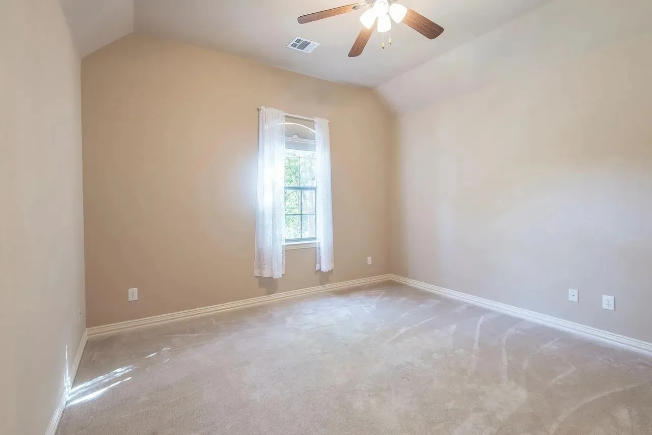Bedroom with vaulted ceiling, neutral carpet flooring, and a window with white sheer curtains