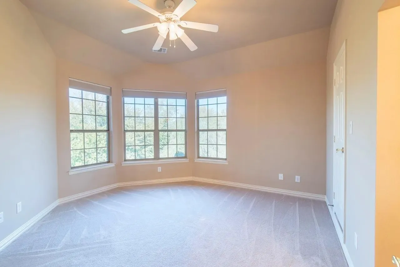 Spacious room featuring a bay window with three large windows, a vaulted ceiling, a ceiling fan, plush carpeting, and neutral paint tones