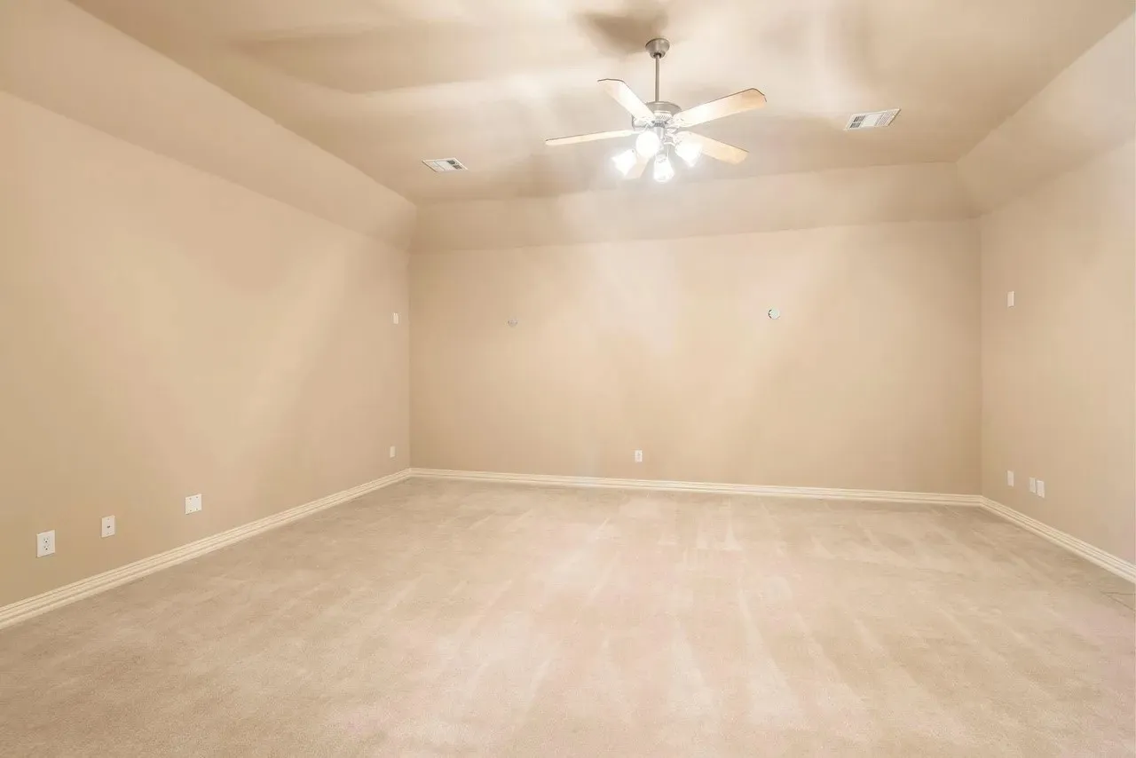 Spacious room featuring neutral carpeting, light beige wall paint, a tray ceiling, and a ceiling fan with integrated lighting
